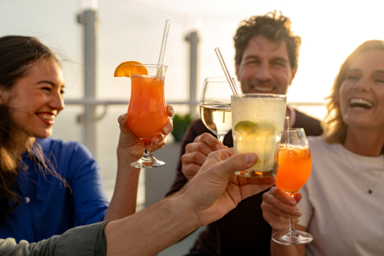 Zwei Frauen, ein Mann sto&szlig;en mit Cocktails an auf einem Kreuzfahrtschiff